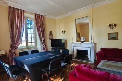 Chambre lumineuse avec murs en toile de Jouy rouge, mobilier classique, table basse et fauteuils près d'une fenêtre.
