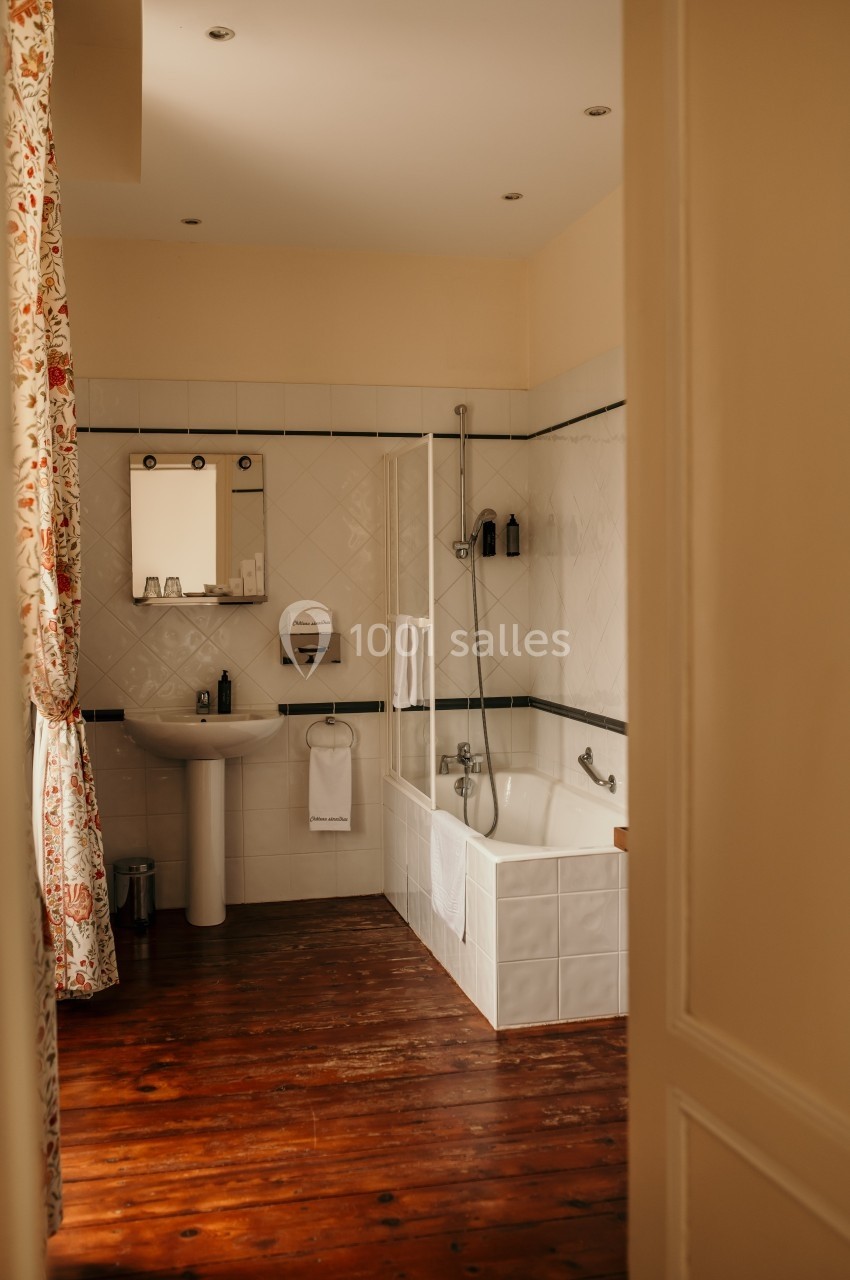 Salle de bain lumineuse avec baignoire, lavabo, miroir, carrelage blanc et sol en bois.