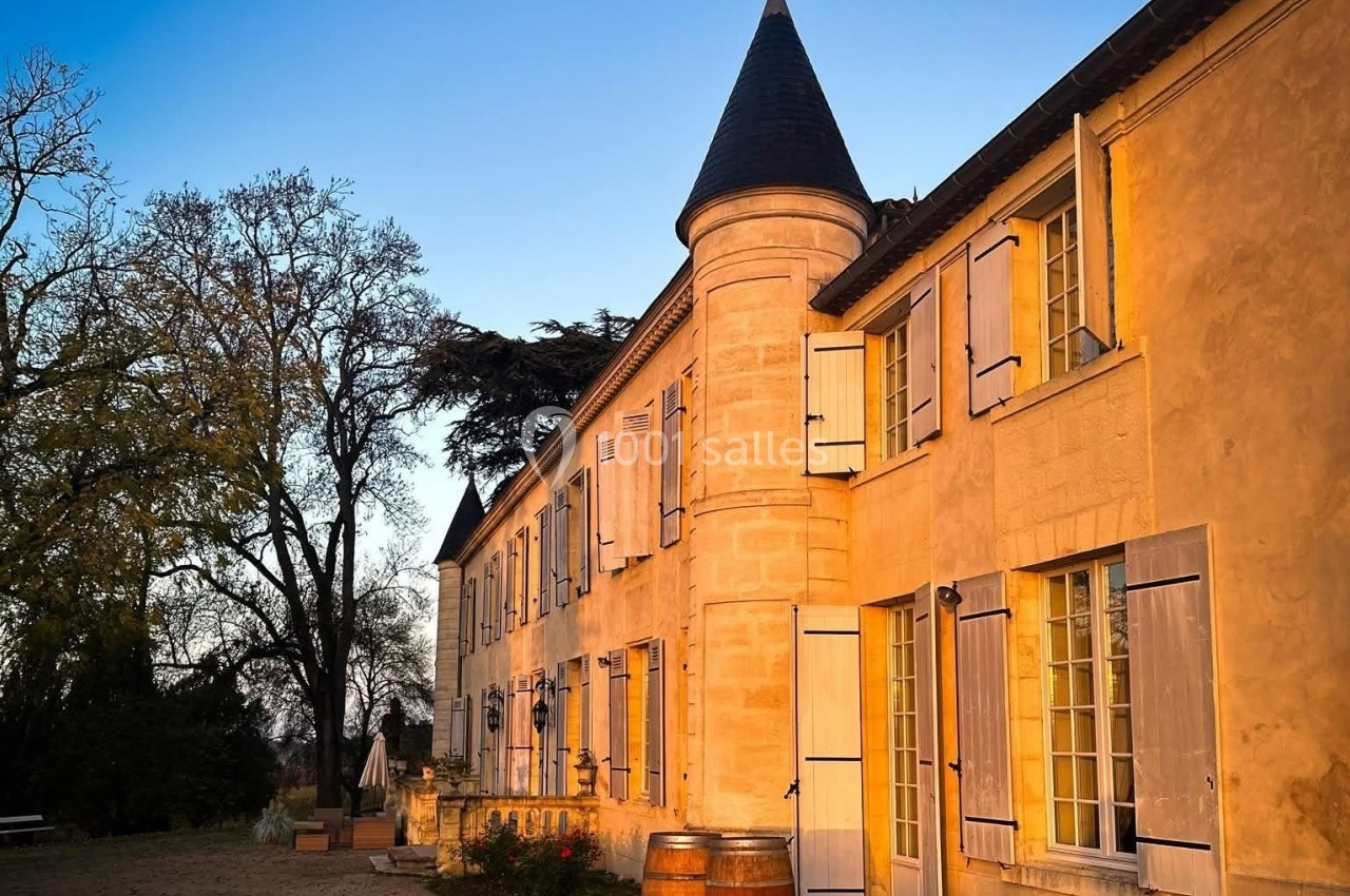 Façade d'un bâtiment en pierre avec des volets ouverts, éclairée par une lumière chaude au coucher du soleil.