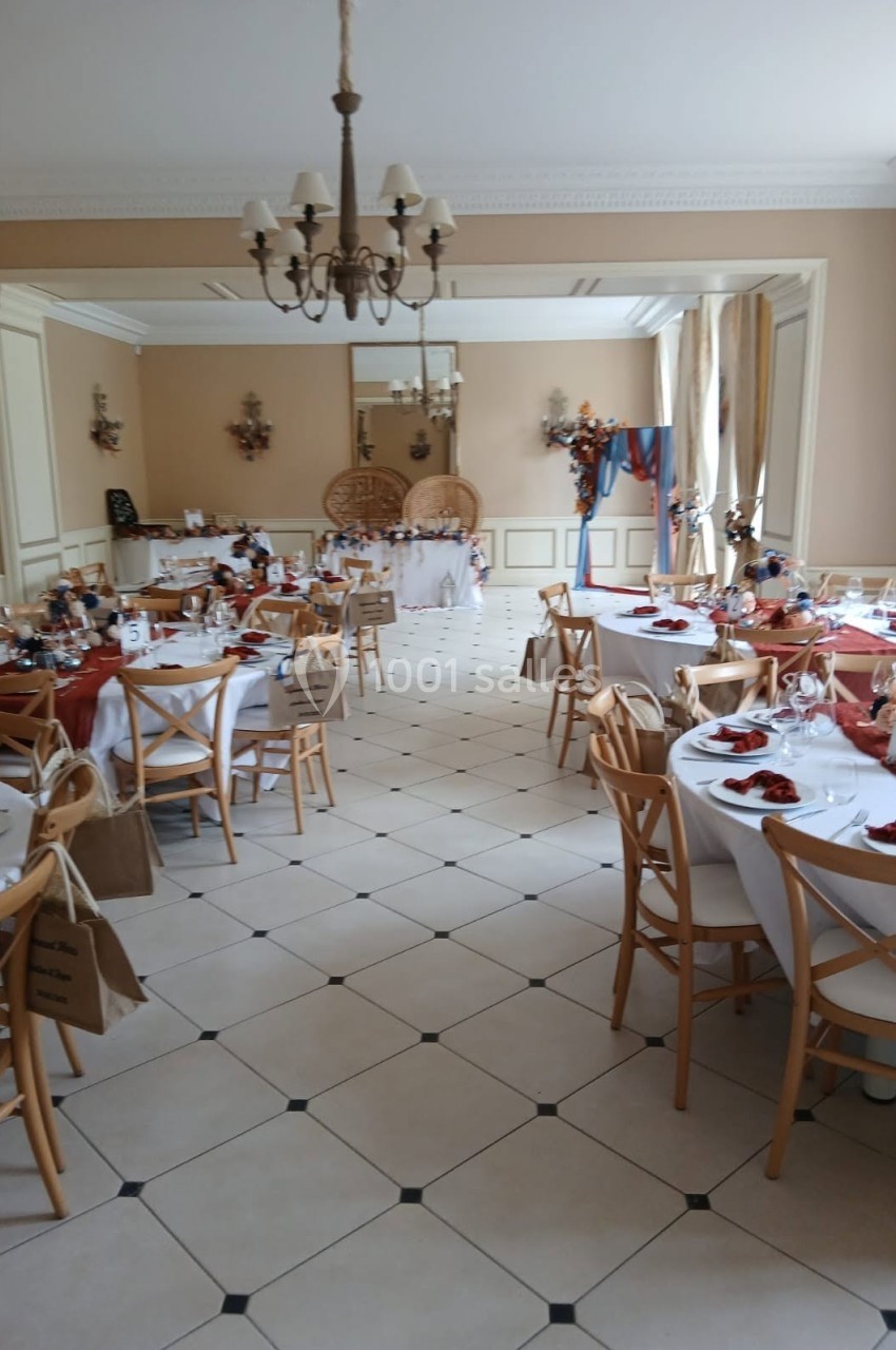 Salle décorée pour un événement, avec tables dressées, nappes blanches, chaises en bois et décorations colorées.