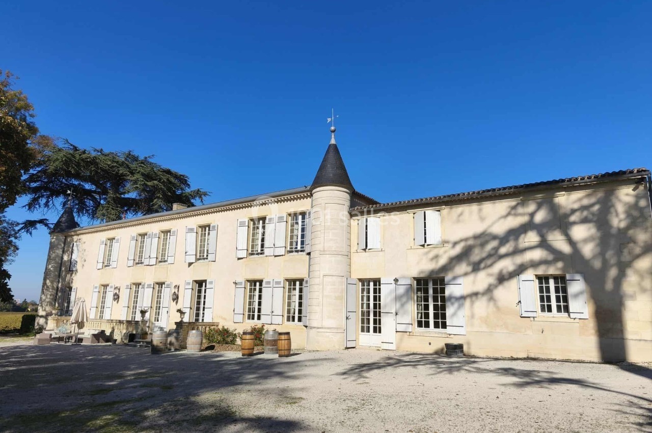 Façade d'un bâtiment ancien en pierre avec des volets blancs, sous un ciel bleu dégagé.