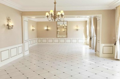 Façade claire avec volets blancs, lanterne en fer forgé et jardinières de fleurs roses en premier plan.