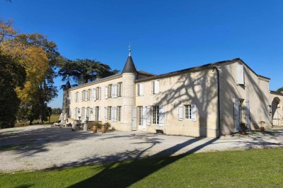 Façade claire avec volets blancs, lanterne en fer forgé et jardinières de fleurs roses en premier plan.