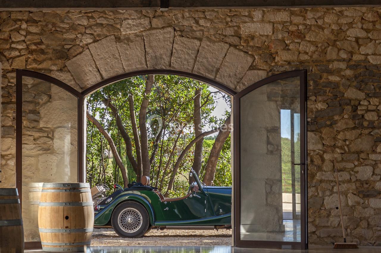 Voiture ancienne verte garée devant une porte voûtée ouverte, dans un bâtiment en pierre avec tonneaux en bois.
