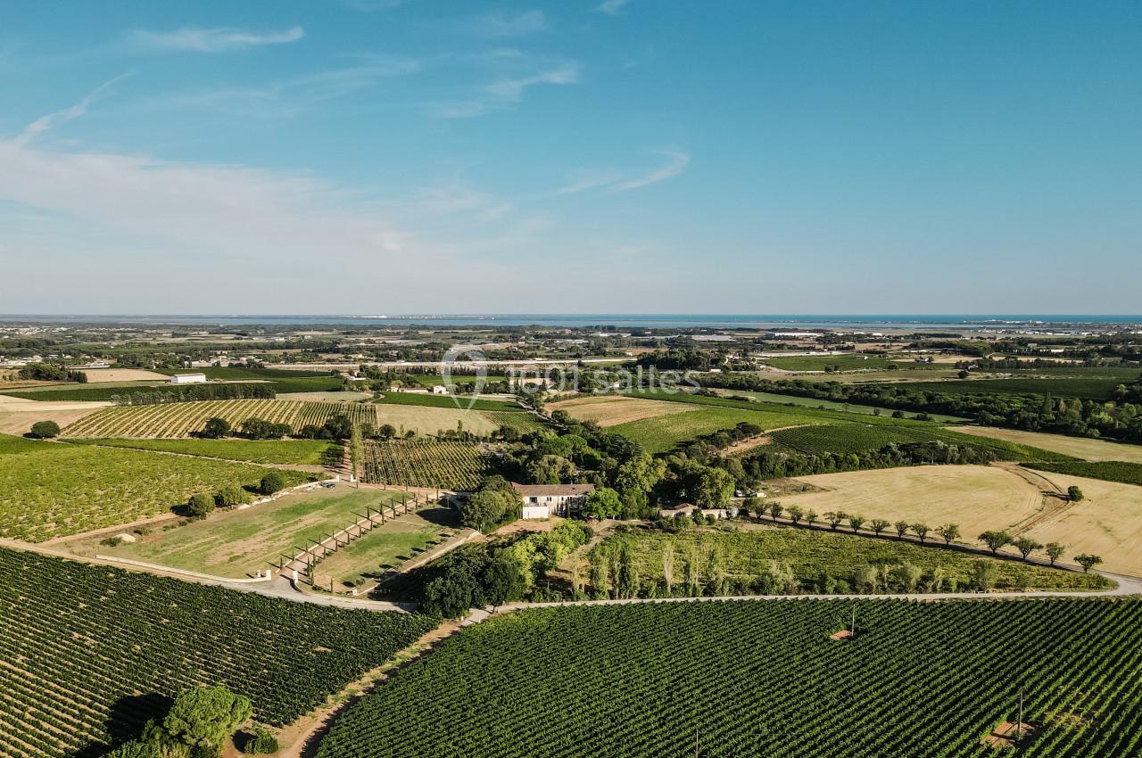 Vue aérienne d'un paysage rural avec des champs cultivés, des vignobles et quelques bâtiments sous un ciel dégagé.