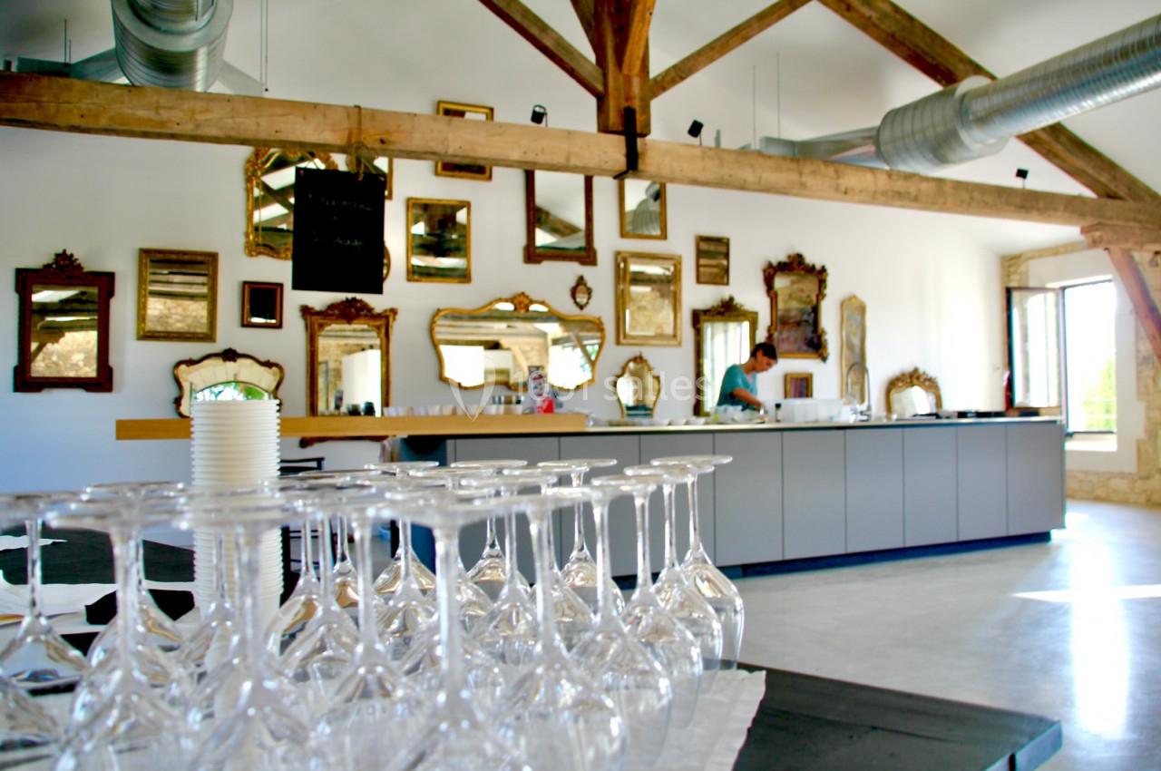 Salle lumineuse avec des murs ornés de miroirs, un comptoir moderne et des verres à pied alignés au premier plan.