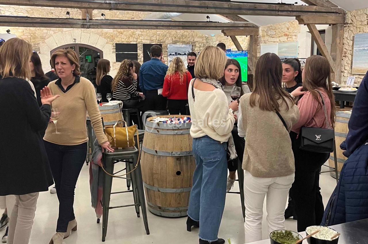 Des personnes discutent dans une salle lumineuse avec des poutres apparentes, un buffet de légumes colorés au premier plan.