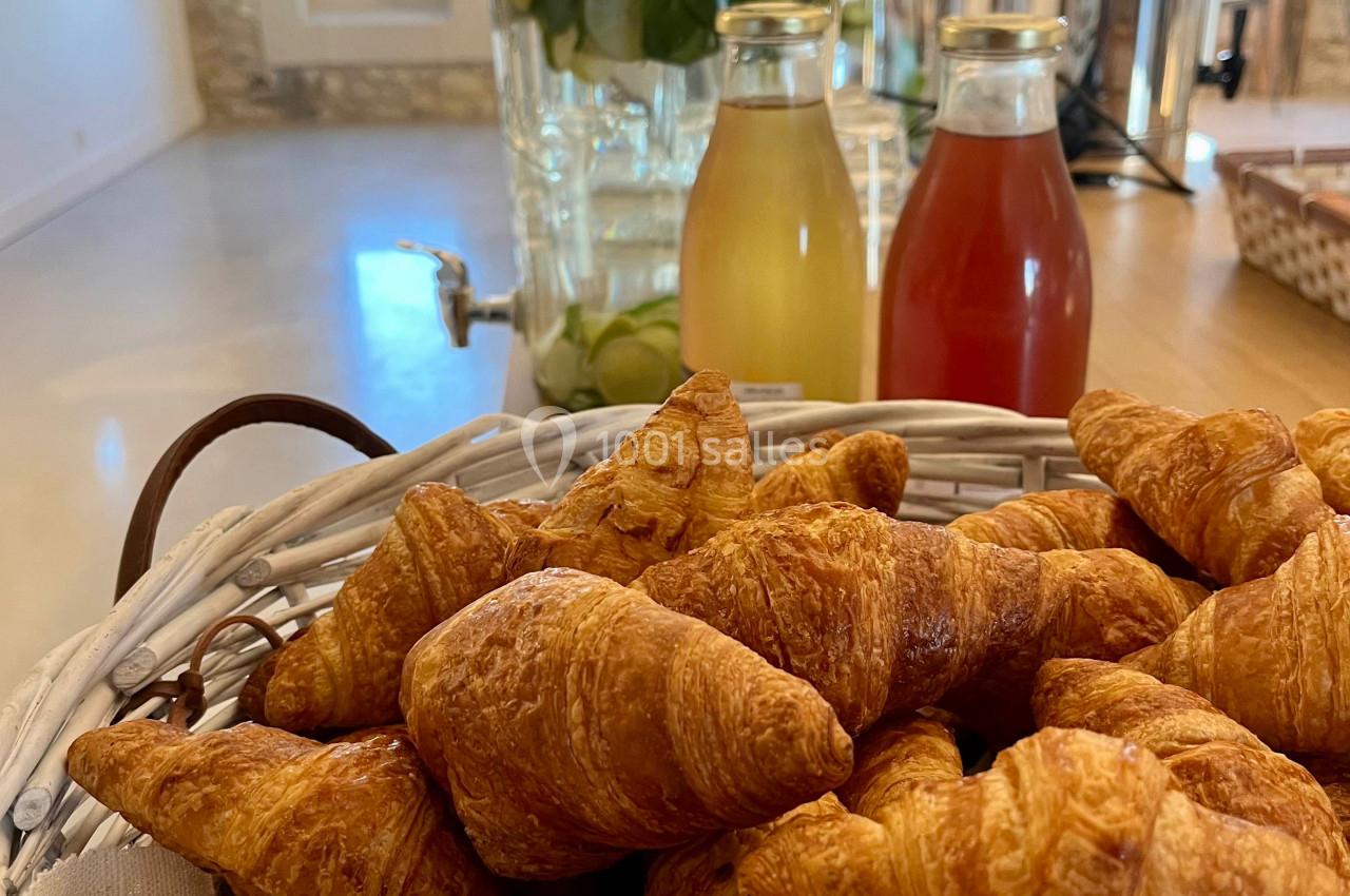 Panier de croissants frais au premier plan, avec des boissons et un grand bocal d'eau infusée en arrière-plan.