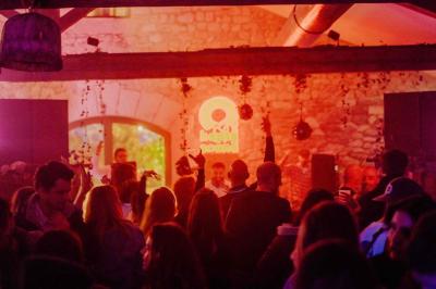 Personnes assises à des tables en plein air dans un jardin, entourées de verdure et de guirlandes lumineuses suspendues.