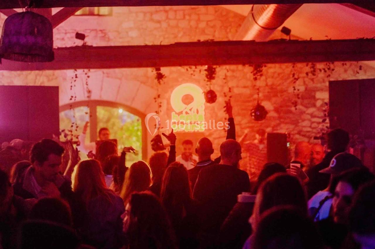 Foule dans un espace intérieur faiblement éclairé avec un éclairage rouge et un logo lumineux en arrière-plan.