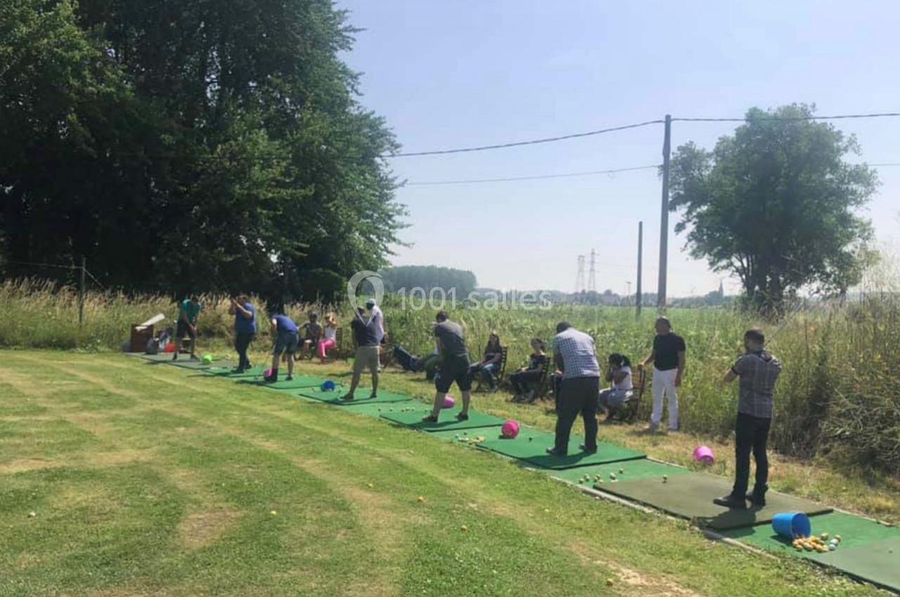 Des personnes s'entraînent au golf sur un terrain en plein air, avec des tapis de practice et un paysage verdoyant.