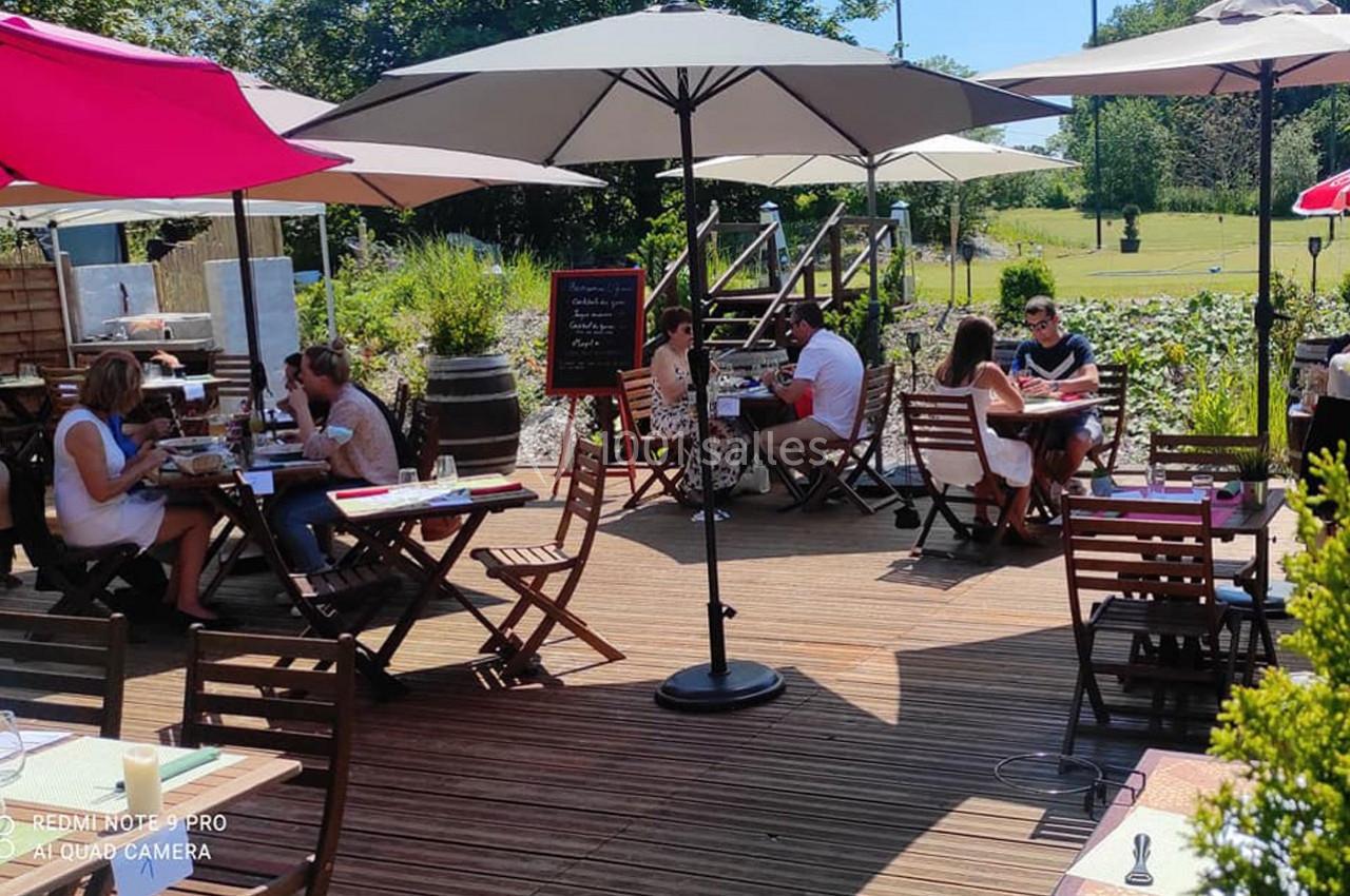Terrasse en bois d'un restaurant avec des tables, des parasols et des clients profitant d'un repas en extérieur.