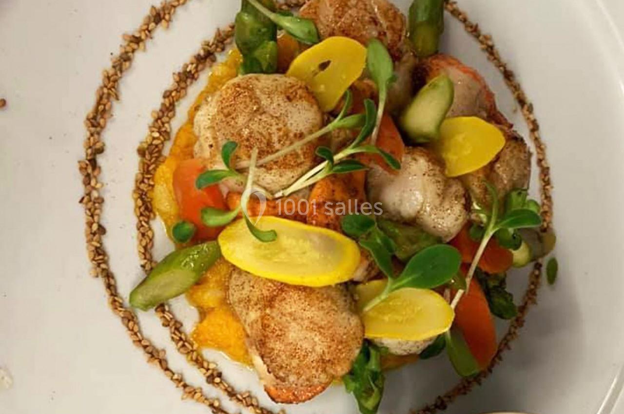 Assiette de noix de Saint-Jacques servies sur un lit de purée, accompagnées de légumes colorés et de jeunes pousses.