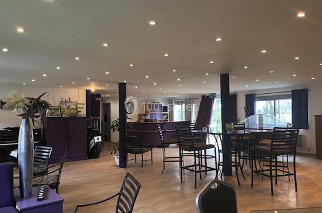 Salle lumineuse avec des tables et chaises en métal, décorée de tons violets et éclairée par des spots au plafond.