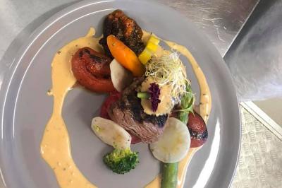 Table dressée en extérieur avec nappes blanches, fleurs en centre de table, parasols roses et verdure en arrière-plan.