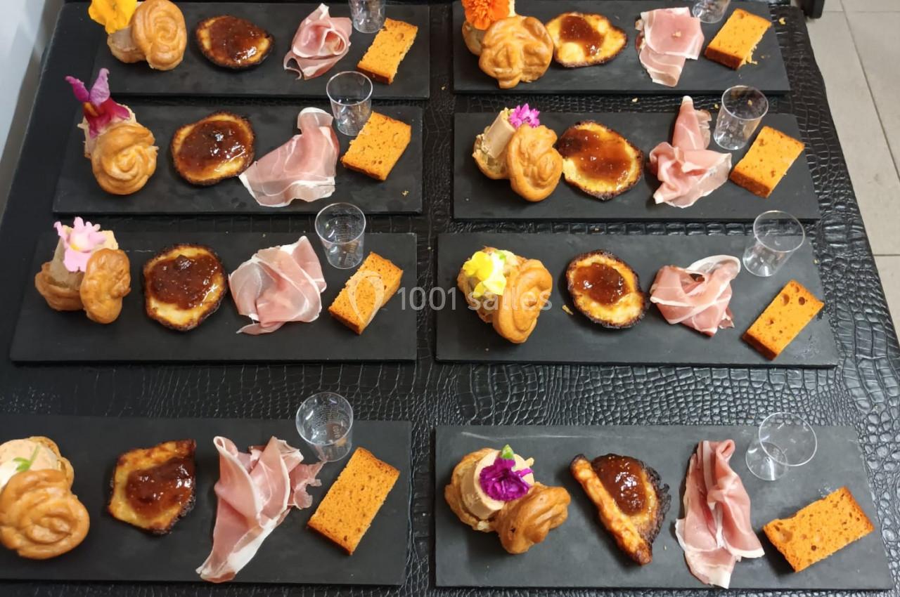 Assiettes de dégustation disposées sur des ardoises, contenant charcuterie, fromage, biscuits et décorations florales.