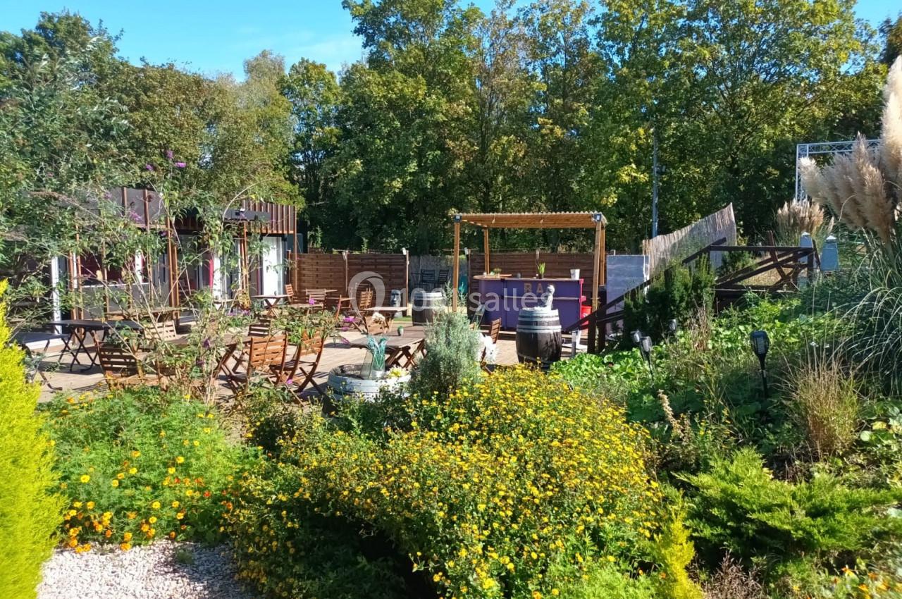 Jardin aménagé avec des fleurs, des tables en bois, un bar extérieur et des arbres en arrière-plan.
