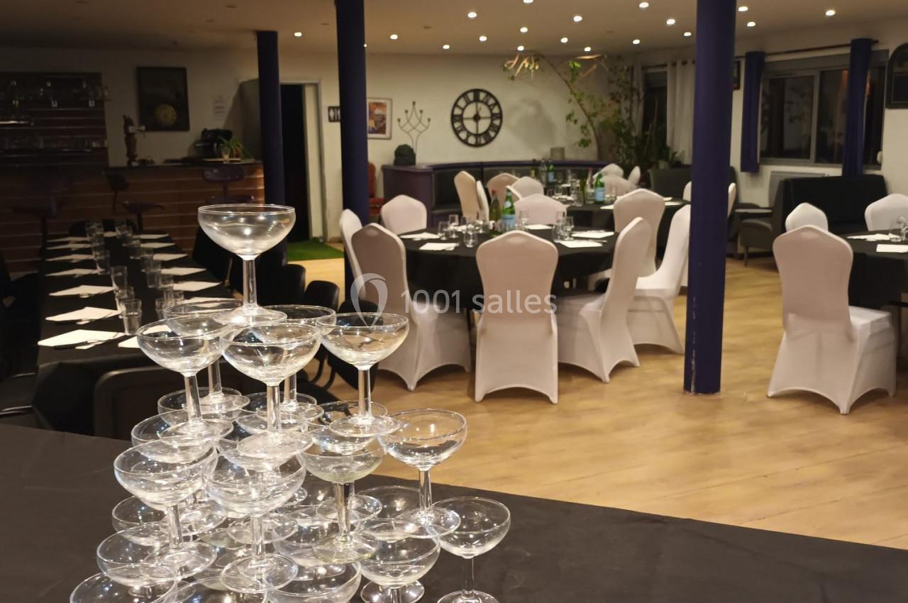 Salle de réception décorée avec des tables dressées et une pyramide de coupes à champagne au premier plan.