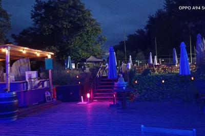 Table dressée en extérieur avec nappes blanches, fleurs en centre de table, parasols roses et verdure en arrière-plan.