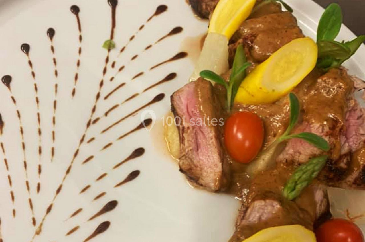 Assiette de viande grillée avec sauce, légumes colorés et décoration de sauce en éventail sur le côté.