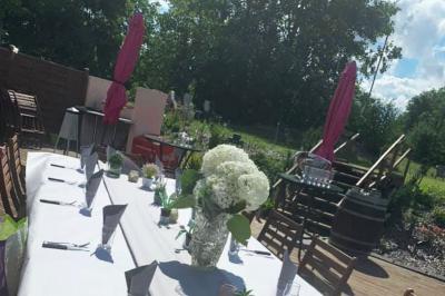 Table dressée en extérieur avec nappes blanches, fleurs en centre de table, parasols roses et verdure en arrière-plan.