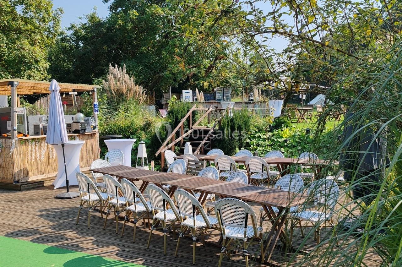 Terrasse en bois avec tables et chaises en rotin, entourée de verdure et aménagée pour un événement en plein air.