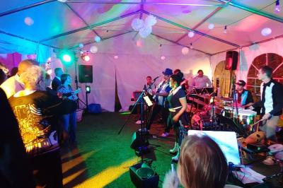 Table dressée en extérieur avec nappes blanches, fleurs en centre de table, parasols roses et verdure en arrière-plan.