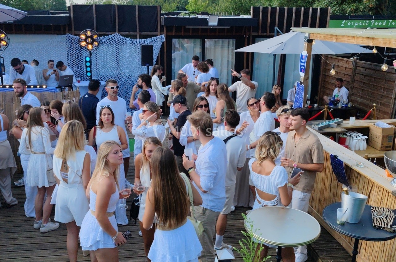 Groupe de personnes en tenue estivale blanche réunies sur une terrasse en bois lors d'un événement en plein air.