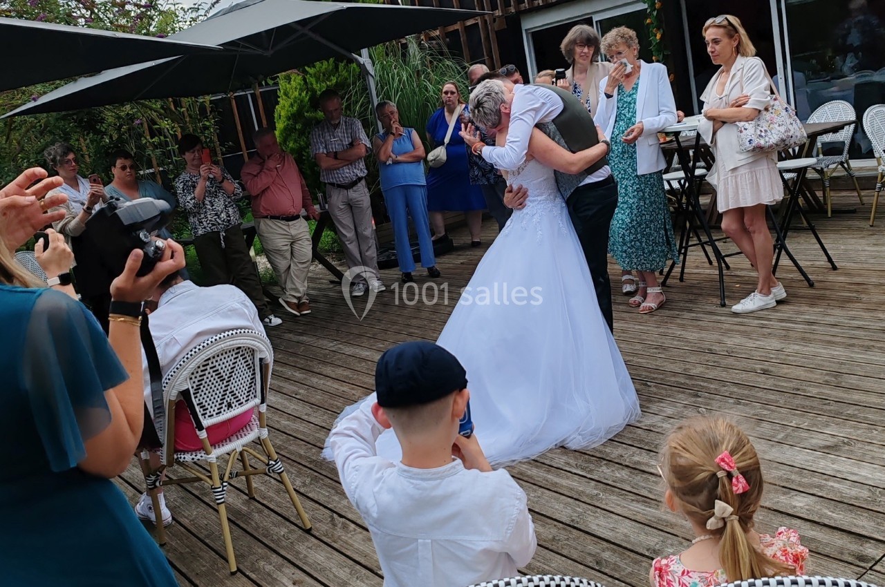 Un couple de mariés danse sur une terrasse en bois entouré d'invités debout et assis.