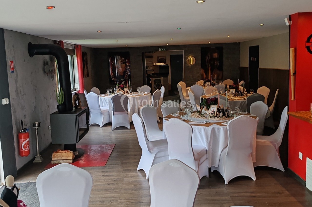 Salle de réception avec tables rondes dressées, nappes blanches et décoration sobre, ambiance chaleureuse.