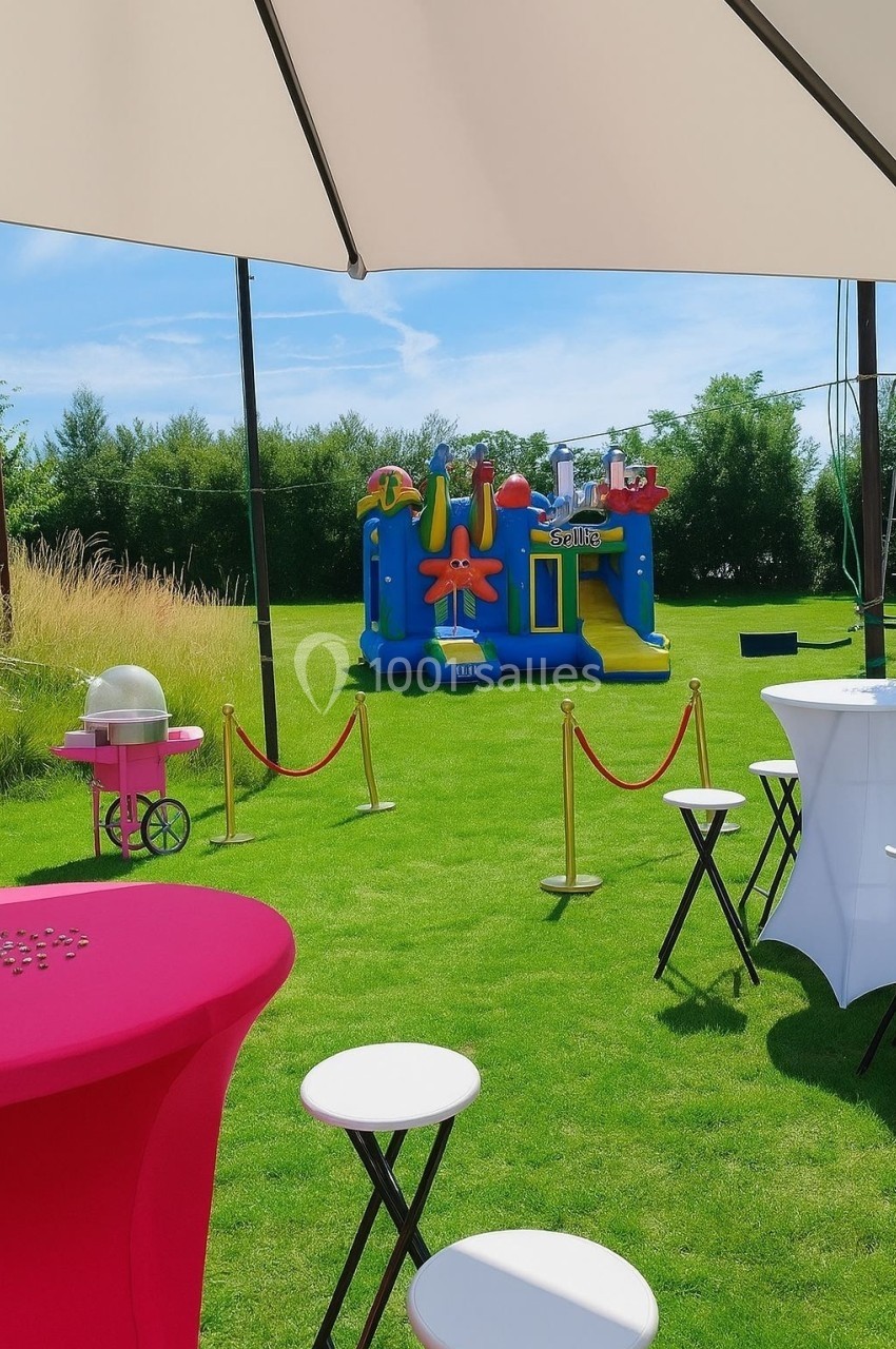Structure gonflable colorée sur une pelouse, entourée de tables hautes et d'une machine à barbe à papa.