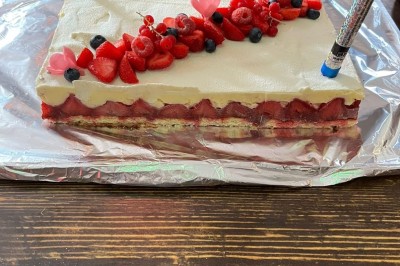 Gâteau rectangulaire décoré de fruits rouges et de cœurs en sucre, posé sur une table en bois.