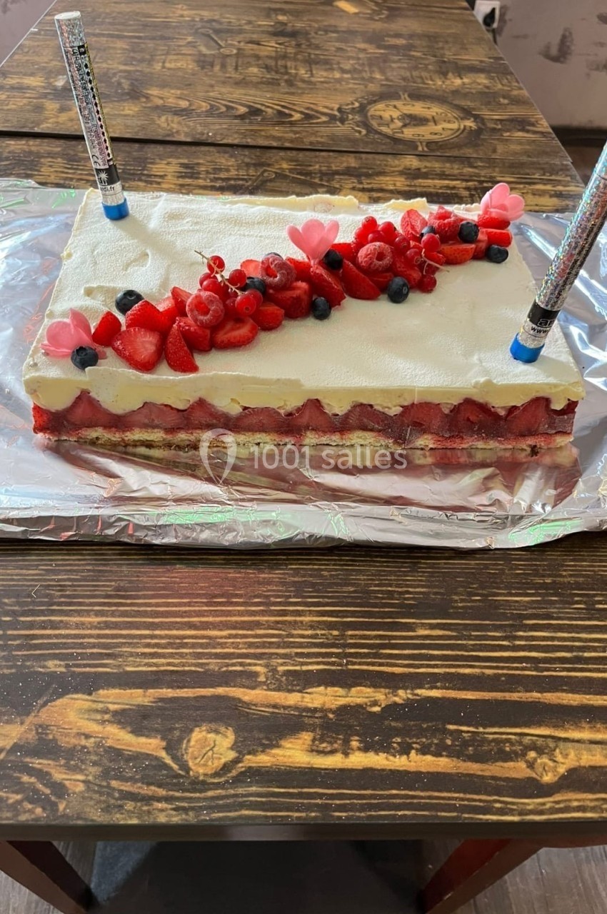 Gâteau rectangulaire décoré de fruits rouges et de cœurs en sucre, posé sur une table en bois.
