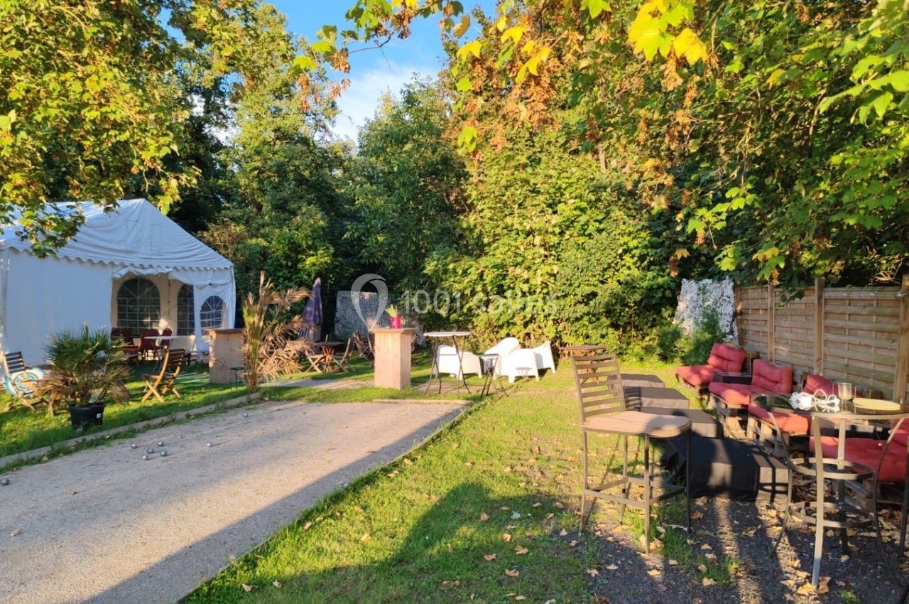 Espace extérieur avec tables, chaises et une tente blanche, entouré de verdure sous une lumière ensoleillée.