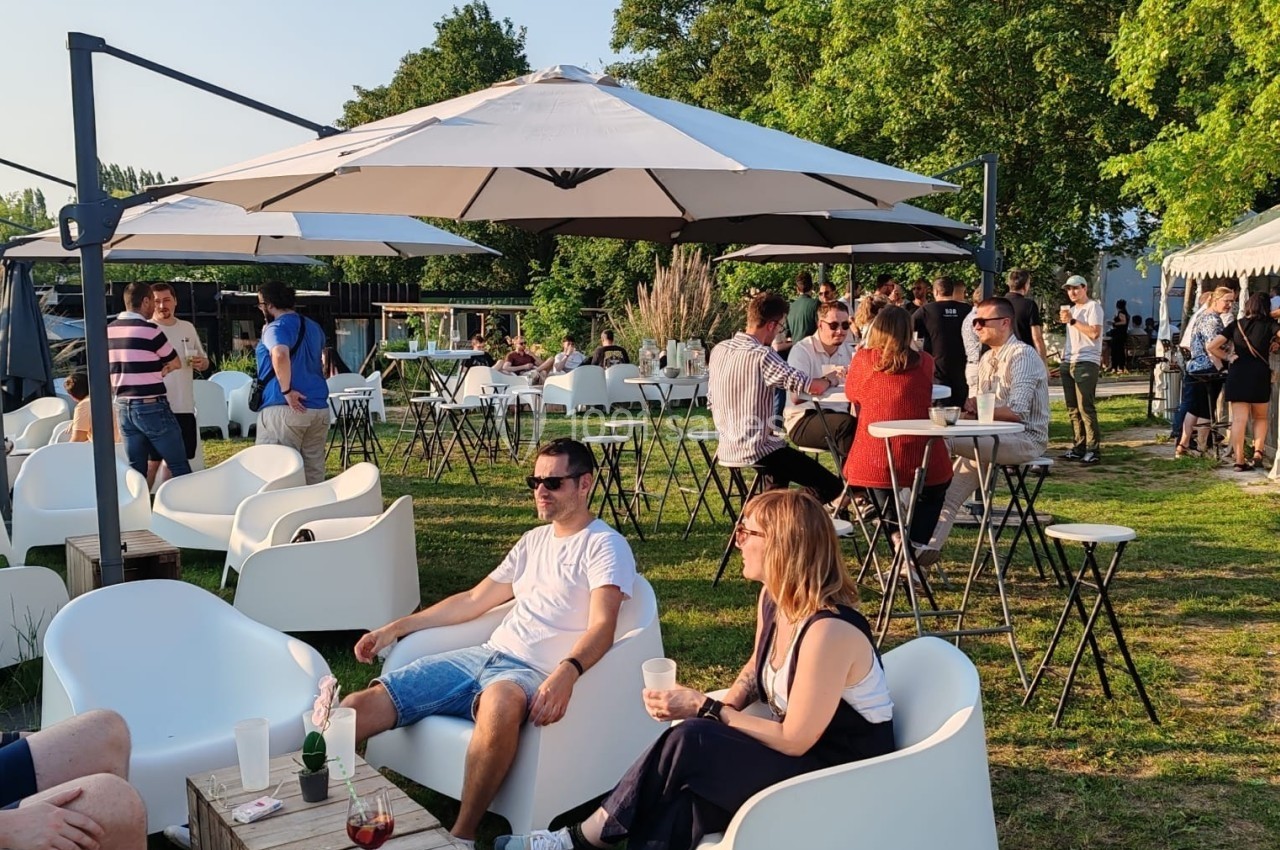Des personnes discutent et se détendent sur des fauteuils et autour de tables en plein air, sous des parasols, par temps…
