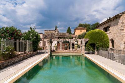 Jardin éclairé de nuit avec piscine, terrasse en pierre et bâtiments entourés de végétation.