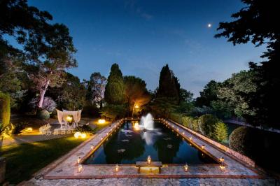 Jardin éclairé de nuit avec piscine, terrasse en pierre et bâtiments entourés de végétation.