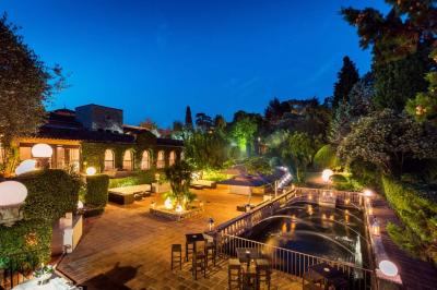 Jardin éclairé de nuit avec piscine, terrasse en pierre et bâtiments entourés de végétation.