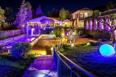 Jardin éclairé de nuit avec piscine, terrasse en pierre et bâtiments entourés de végétation.
