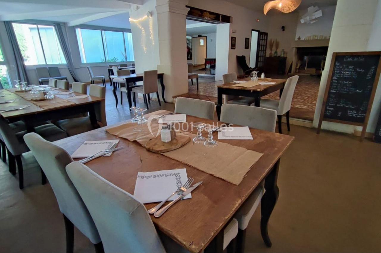 Salle de restaurant lumineuse avec tables en bois dressées, nappes en toile de jute et grande baie vitrée.