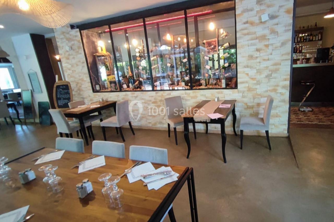 Salle de restaurant moderne avec tables en bois, chaises rembourrées et vue sur une cave vitrée éclairée.