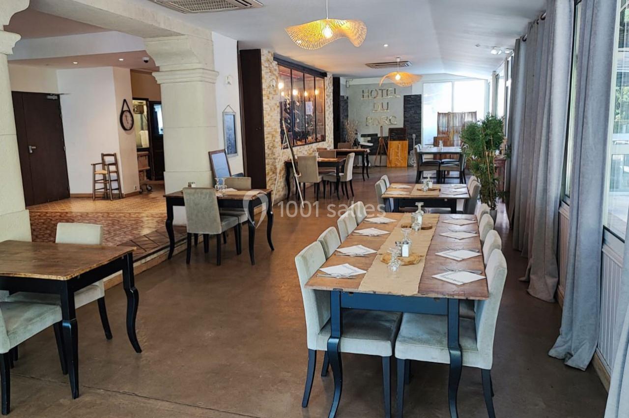 Salle de restaurant lumineuse avec tables dressées, chaises rembourrées et décor sobre mêlant bois et pierre.