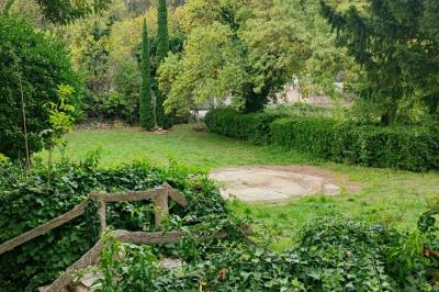 Jardin verdoyant avec pelouse, arbres et buissons, entourant une petite clairière circulaire en béton.