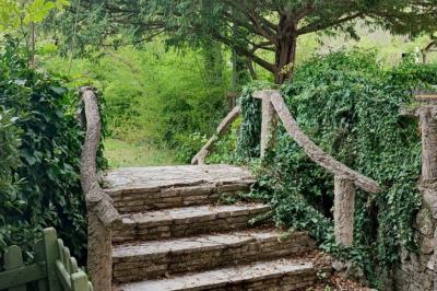 Jardin verdoyant avec pelouse, arbres et buissons, entourant une petite clairière circulaire en béton.