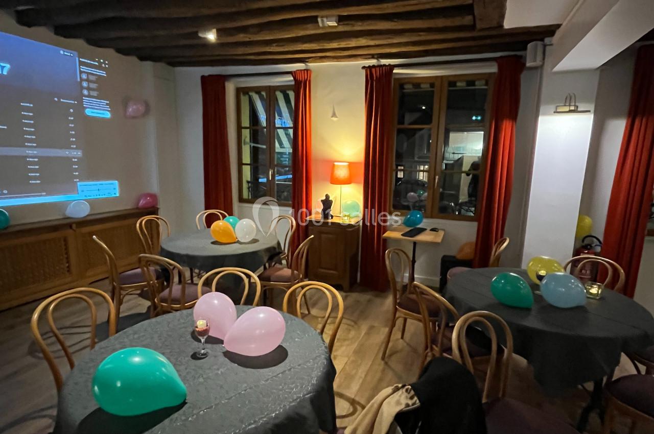 Salle décorée pour un événement avec des tables rondes, des ballons colorés et un éclairage chaleureux.