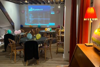 Cour intérieure aménagée avec des poufs colorés, des tables en bois et des guirlandes lumineuses suspendues.