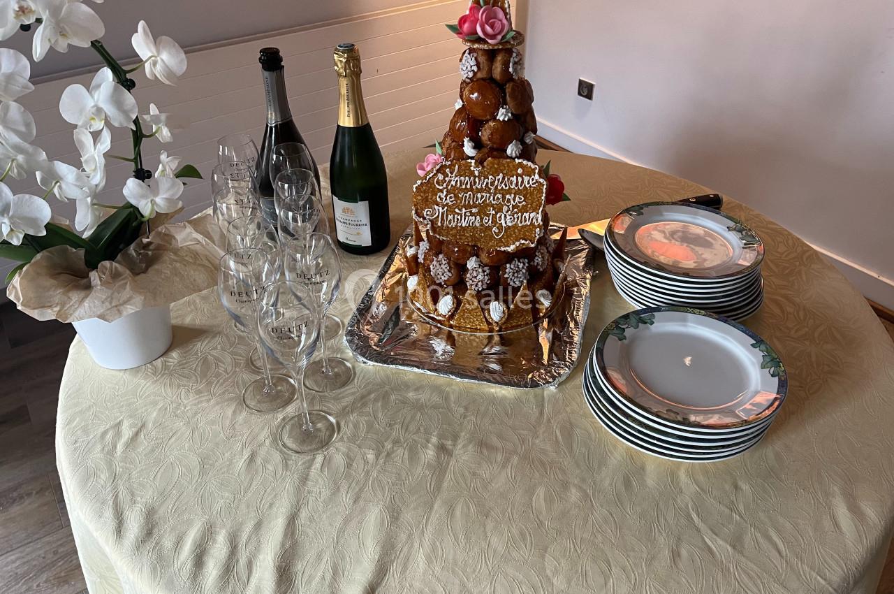 Pièce montée de choux décorée de roses avec des bouteilles de champagne, flûtes et assiettes sur une table dressée.