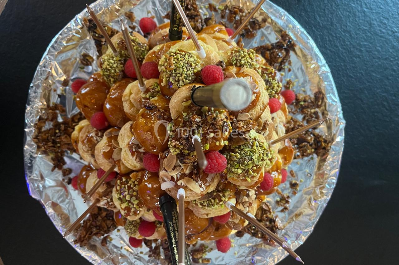 Pyramide de choux garnis de caramel, pistaches, framboises et décorations, présentée sur un support argenté.
