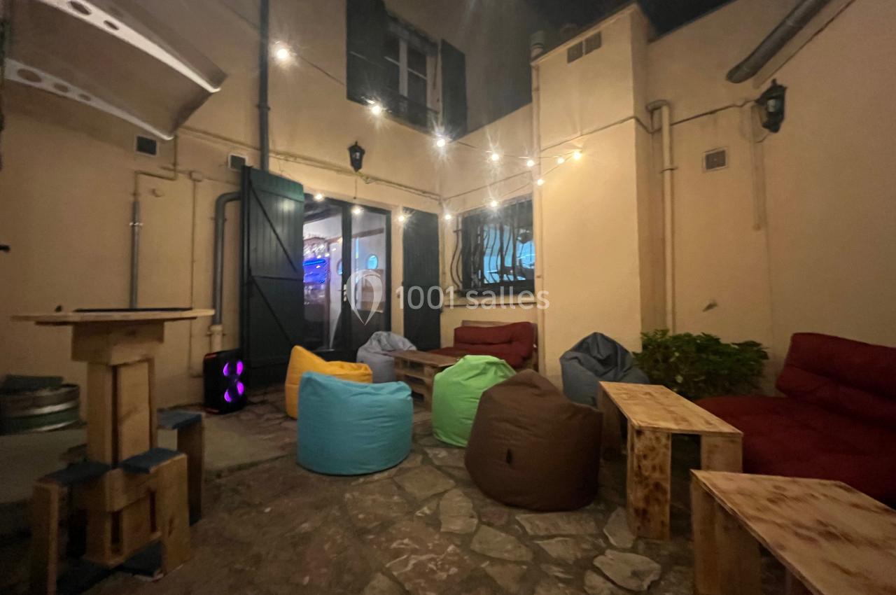 Cour intérieure aménagée avec des poufs colorés, des tables en bois et des guirlandes lumineuses suspendues.