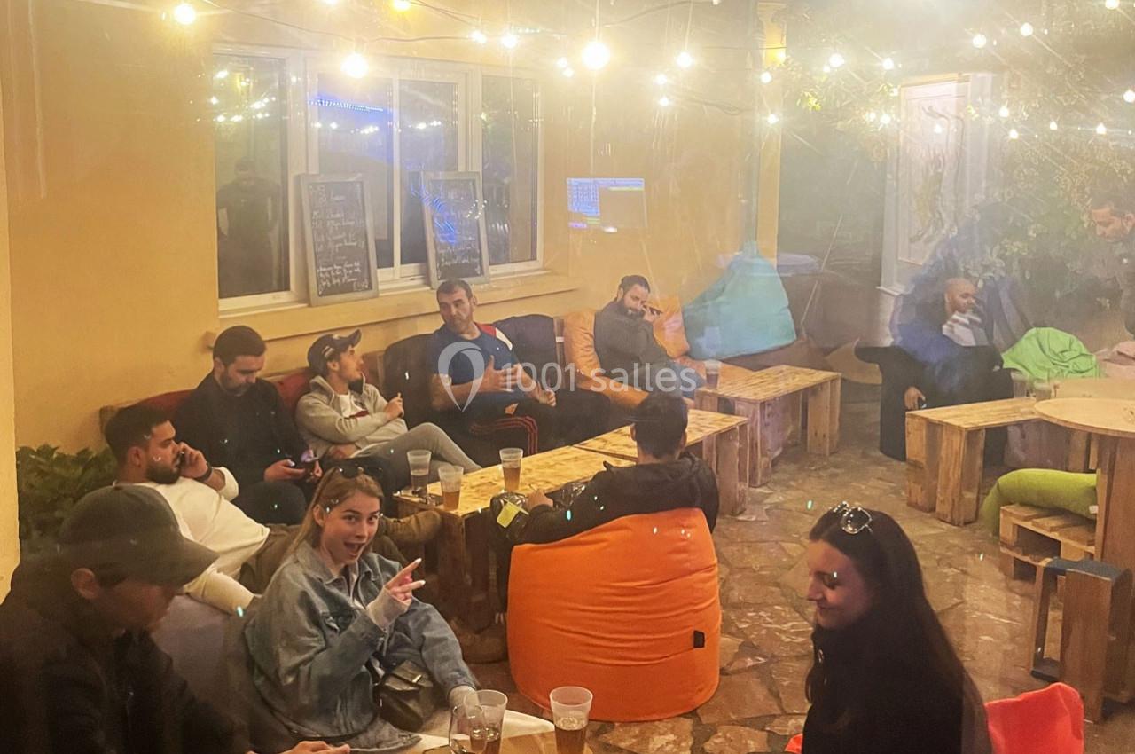 Groupe de personnes assises dans une cour éclairée par des guirlandes lumineuses, discutant et partageant un moment…